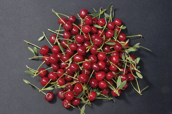 Büyük bir krem çanak kiraz ve petioles ile üst dolu, yanında yeşil yaprakları vardır, beton altında kaba doku siyah bir arka plan üzerinde tüm