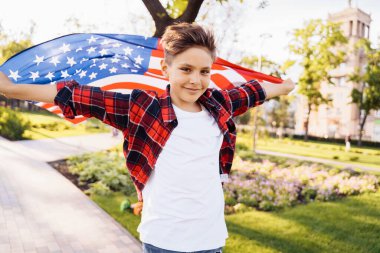 ABD Bağımsızlık Günü. Genç bir Amerikalı ya da beyaz, 8 yaşında, kaykay sürat yapıyor. Amerika 'nın dalgalanan bayrağını tutuyorum. 4 Temmuz 'u kutluyoruz. Sevimli küçük çocuk.
