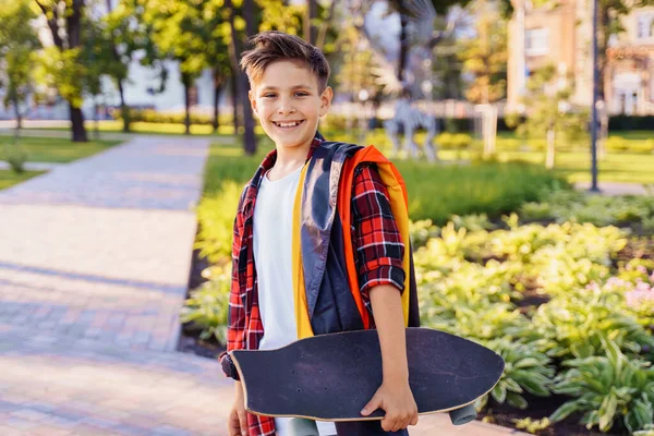 Guy of 9 years old riding skateboard on sunny road in the evening in the city park. Holding fluttering flag of Germany. Happy German day. German language, European education.