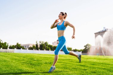 Young professional athlete woman practicing a run on stadium green grass on a sunny morning. Happy with her daily life. Every day increases the speed of her run. clipart