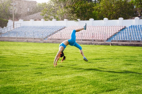競技場では女性アスリートが宙返りをし 屋外で演習を行い 複雑なアクロバティックな演習を行う スポーツと健康的なライフスタイル 新鮮な一日の始まりとレクリエーション — ストック写真