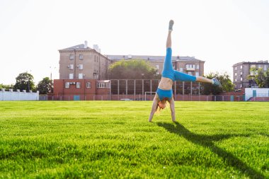 İnanılmaz güzel, atletik kız sıcak bir yaz akşamında spor stadyumunda egzersiz yapıyor. Ellerinin üstünde baş aşağı duruyor..