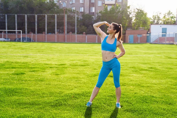 Athletic muscled young woman in a sports wearing doing fitness exercises. Fitness woman posing at the stadium. Healthy athletic lifestyle.