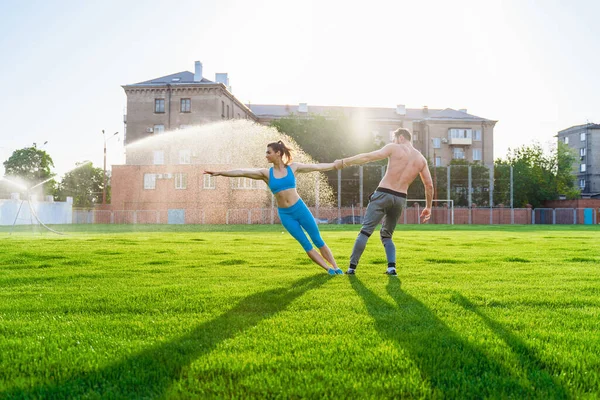 公園やフィールドスタジアムでアクロヨガをする若いカップルに適しています 男は草の上に立って 手に自分の女性のバランスをとる 幸せな スポーツ若い選手 — ストック写真
