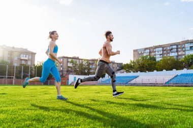 Stadyumda koşan erkek ve kadın sporcular. Yetişkinler için sağlıklı spor aktiviteleri. Eğitimdeki genç atletler, koşucu egzersizleri. Çimlerin üzerindeki stadyumda koşucuların dinamik koşusu.