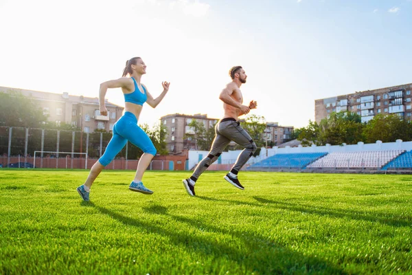 競技場で走っているスポーツマンと女性 大人のための健康的なスポーツ活動 練習中の若い選手 ランナー運動中 芝生の上のスタジアムでのスプリンターの動的実行 — ストック写真