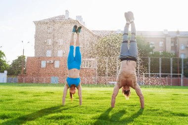 Ellerinin üstünde baş aşağı duruyorlardı. Güçlü, kaslı, şişirilmiş sporcular. Kafkas uyruklu bir çift genç sporcu futbol sahasında duruyor ve farklı fiziksel egzersizler yapıyor..
