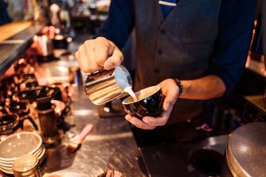 Kahveci ellerinin kahve espressoya süt katıp kapuçino ya da latte yaptığı yakın plan çekimler. Profesyonel bir barmen tezgahta ilham kaynağıyla kahve hazırlıyor..