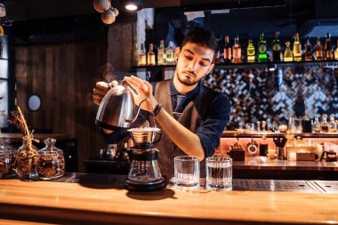 Yumuşak, sarı akşam lambası olan popüler bir kafede profesyonel bir barista, kahve çekirdeklerine metal çaydanlıktan sıcak su döküyor. Kahve yapmak için alternatif bir yol. Kahve filtresi.