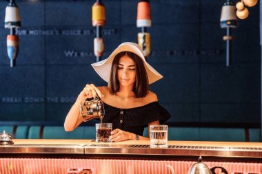 Güzel, zarif, sofistike bir kadın barda tek başına oturuyor. Şeffaf bir çaydanlıktan bardağına filtre döküyorum. Bar tezgahından güzel atmosferik sarı ışık..