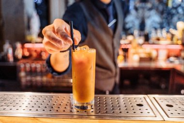 Yakışıklı esmer barista bir restoranın barında bir içki. Kokteyle buz ekleyerek bir kahve ve portakal suyu karıştırıyorum. İçme çubuğu takıyor. Liqiud ile yakın çekim cam..