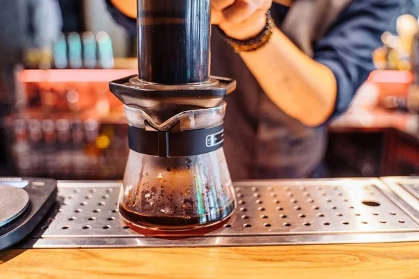 Alternative method of brewing coffee. Close up of hands of attractive young barista using press. Gently presses on flask, passing coffee liquid through filter. Coffee without milk and sugar.
