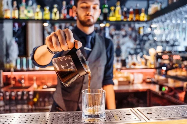 Kafkas sakallı genç bir erkek baristanın Kalita Wave Dripper kahve filtresinin içine kahve koymasına yakın çekim. Dükkanda dijital ölçekte kahve zeminini ölçtükten sonra sıvı yapmak. Koyu renk üniforma giyiyor..