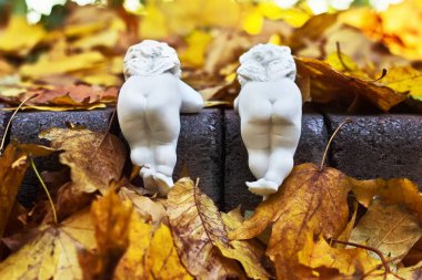 Funny white ceramic angels with small wings are back view in autumn park. clipart