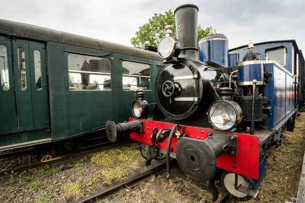 in an old train station there is an old steam train with a large oil lamp in front of his chimney