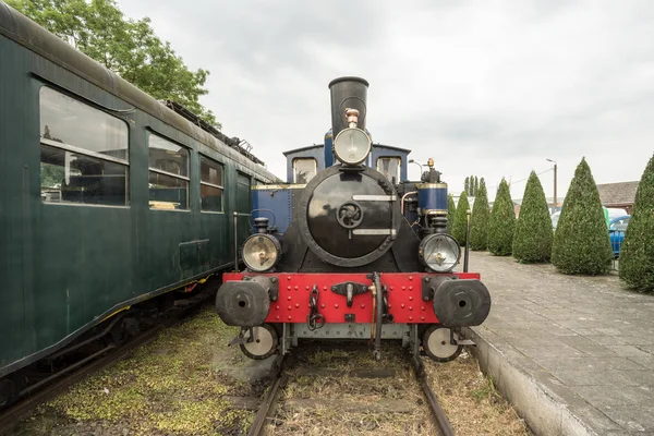 in an old train station there is an old steam train with a large oil lamp in front of his chimney