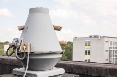 Endüstriyel bölgedeki yüksek bir binanın çatısında vantilatörler var.