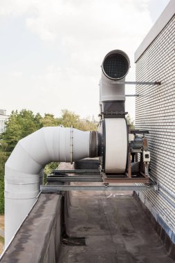 Endüstriyel bölgedeki yüksek bir binanın çatısında vantilatörler var.