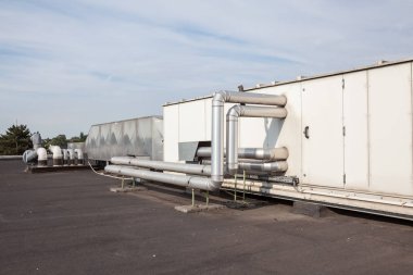 Endüstriyel bölgedeki yüksek bir binanın çatısında vantilatörler var.