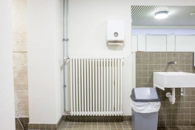 bir kamu tuvaletinde asılı beyaz bir lavabo ve bir radyatör bir duvara
