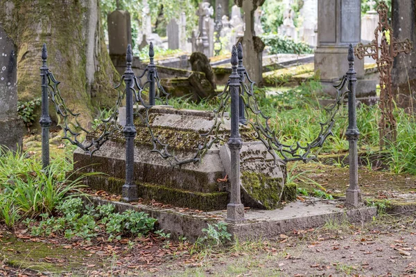 Eski bir mezarlıkta, paslı eski zincirlerle mermer kazıkları olan bir mezar var..