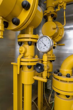 Büyük bir binanın önünde sarı vanalı doğal gaz kabini var.