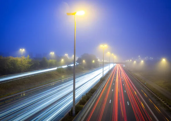 On a foggy morning along the highway with street lights and light stripes of transport