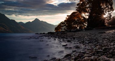 Küçük kayalar yalan görkemli dağlar ve bulutlu gökyüzü arka plan üzerinde sakin Nehri'nin kıyısında akşam tarihinde South Island, Yeni Zelanda