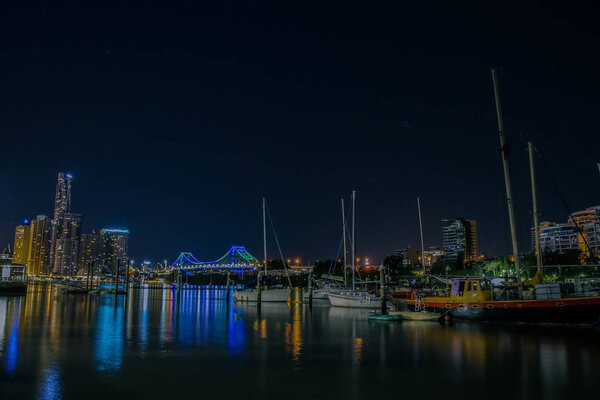 Small vessels floating on surface of calm water on background of modern illuminated city and night sky in Brisbane, Australia