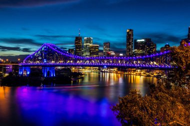 Brisbane sahili ile ışıklı mor köprü ve sarı parlayan ışıklar ve gökdelen günbatımı arka plan üzerinde modern beldesi görüntüleyin
