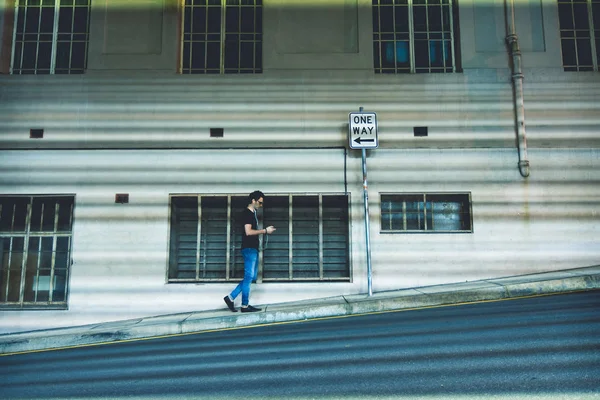 Side view of person with sunglasses listening music and walking on avenue near building in Brisbane, Australia