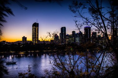 Cityscape modern highrise binaların ışıkları günbatımı zamanı, Brisbane sakin nehir su üstünde