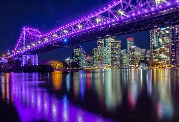 Perspective view of glowing bright bridge above city river giving reflection in night time, Brisbane