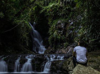 Arkadan kaya üzerinde oturan ve Gold Coast, Avustralya'da görkemli şelale manzaranın rahat kıyafet giyen görünüşü