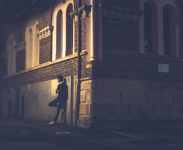 Side view of person leaning on wall of house in avenue and looking away at night in Brisbane, Australia