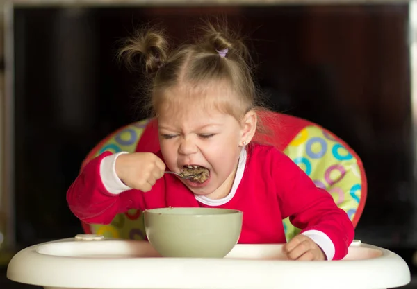 Portrait de petite fille mangeant du porridge à l'aide d'une cuillère assise dans une chaise d'alimentation — Photo