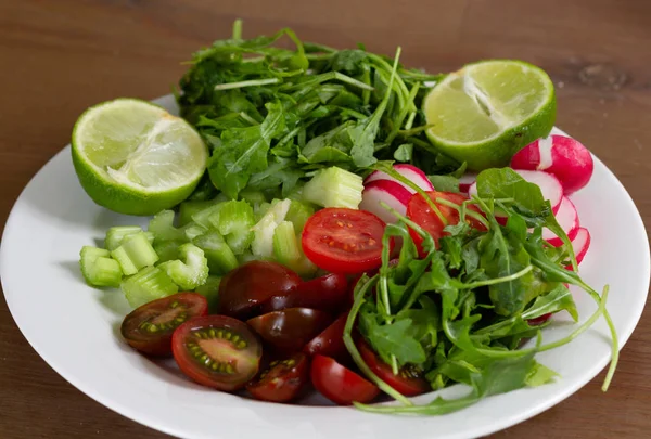 Fresh vegetables as tomato, radish, sliced celery, rosemary and lime on white plate — Stock Photo, Image