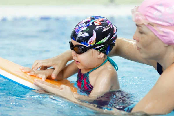 Küçük kız ve annesi yüzme havuzunda float board ile excercises yapma