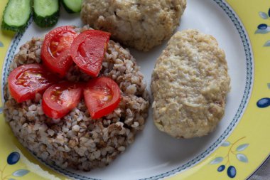 Domates ve salatalık ile süslenmiş tabakta pişmiş karabuğday ve köfte