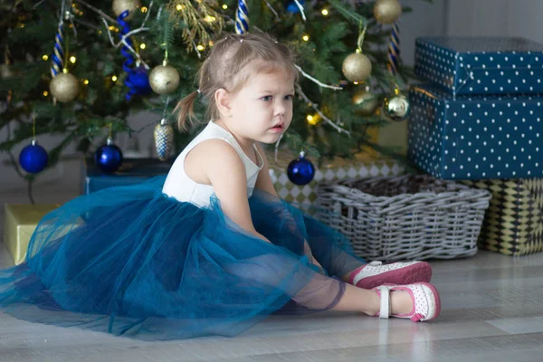 Criança irritada sentada no chão perto da árvore de natal e caixas — Fotografia de Stock