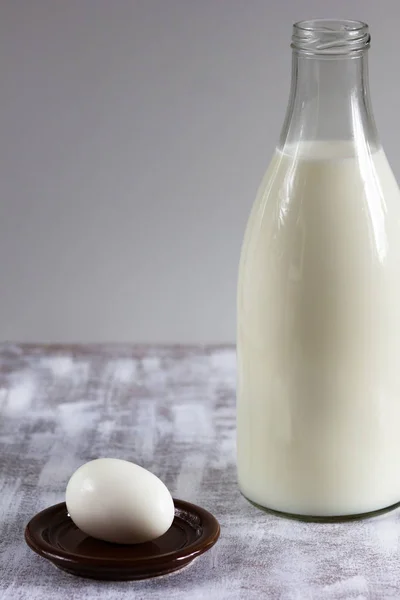Бутылка молока и одно приготовленное яйцо на белом фоне — стоковое фото
