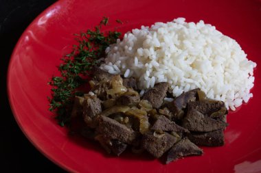 Siyah arka plan üzerinde kırmızı plaka üzerinde pişmiş karaciğer ve pirinç