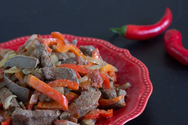 Foie cuit avec des légumes sur plaque rouge sur fond noir — Photo