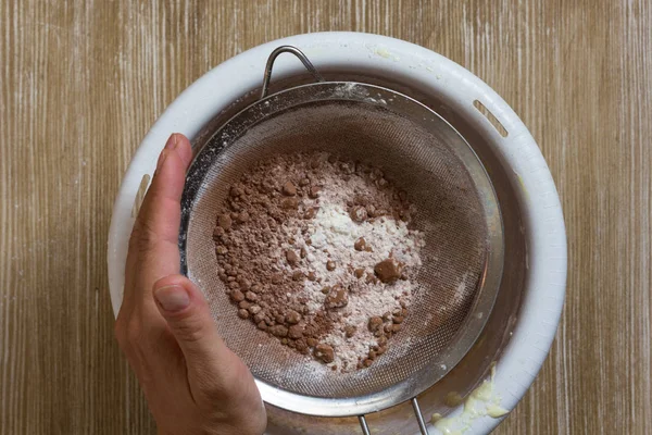 Hand of woman holding sifter with flour, cocoa powder during sifting