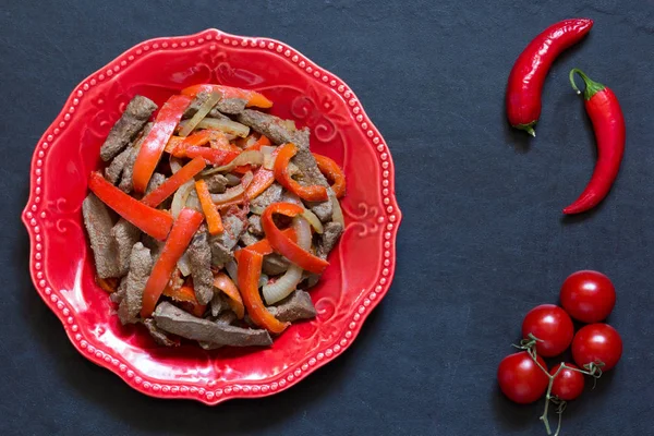 Draufsicht auf gekochte Leber mit Gemüse auf rotem Teller auf schwarzem Hintergrund — Stockfoto