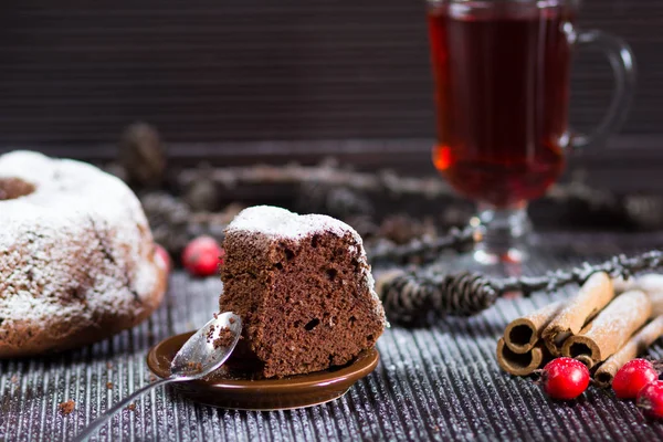 Кусок рождественского шоколадного торта с сахарным порошком на деревянном столе со стаканом красного чая и палочками корицы — стоковое фото