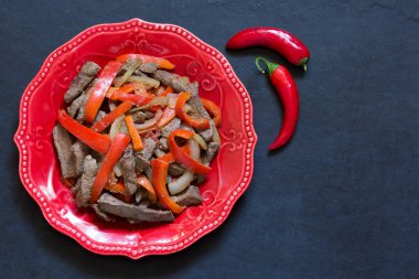 Kırmızı tabakta siyah arka planda sebzeli ciğer manzarası