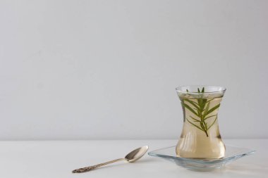 Rosemary tea in Armudu glass with branch of rosemary in it and spoon on the table on white background clipart