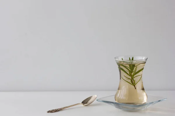 Rosemary tea in Armudu glass with branch of rosemary in it and spoon on the table on white background — Stock Photo, Image
