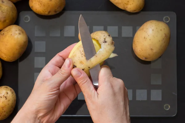 Vrchní pohled na ženu ruční loupání syrové brambory s nožem na černém pozadí — Stock fotografie